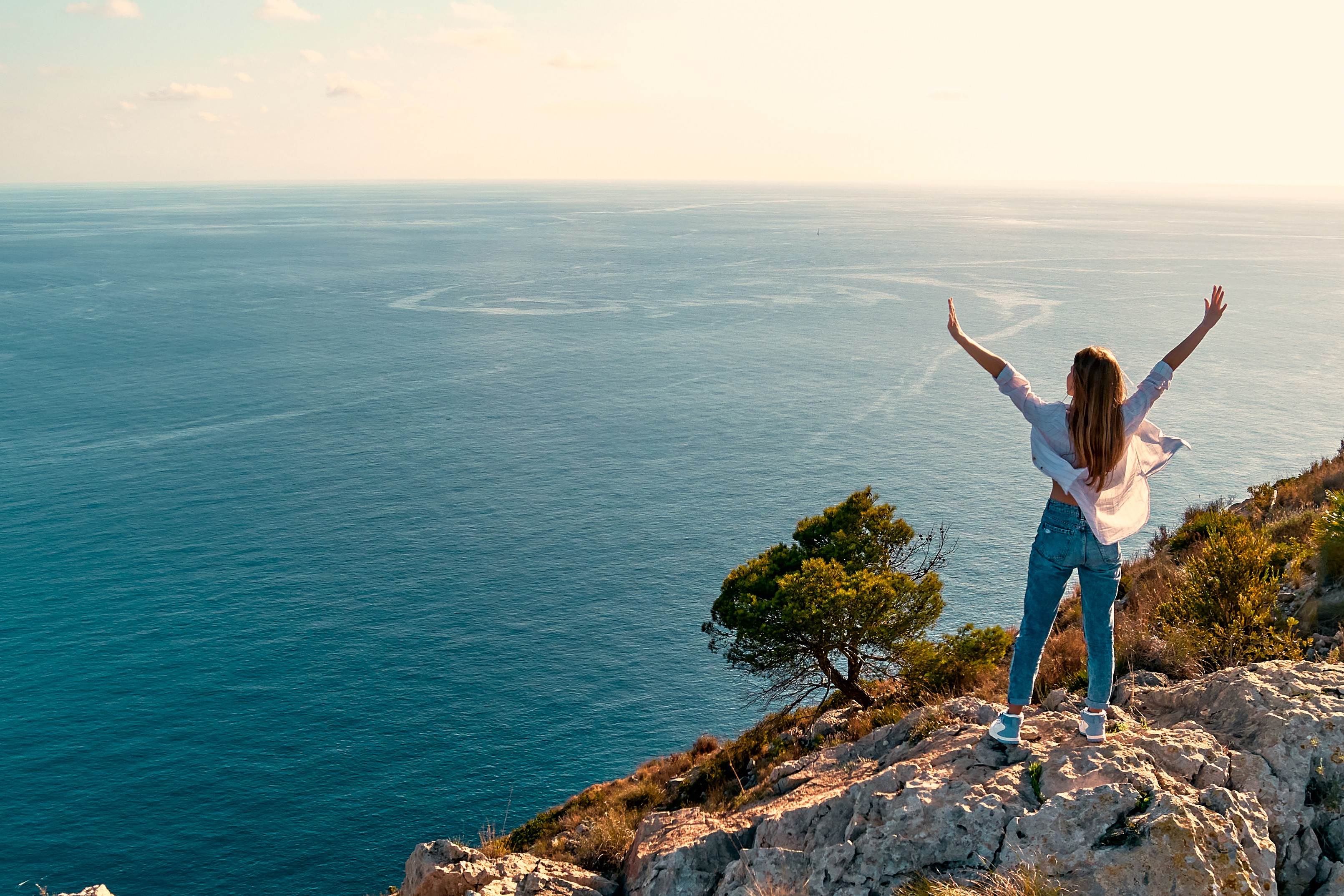 Femme les bras levés face à la mer depuis une falaise, symbole de liberté et de nouveau départ après lasérothérapie à Sherbrooke